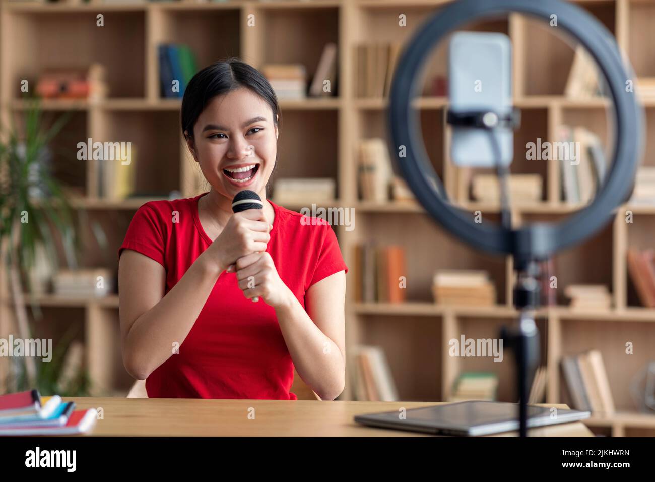 Cheerful pretty young japanese female superstar singing at microphone, shooting blog on smartphone Stock Photo