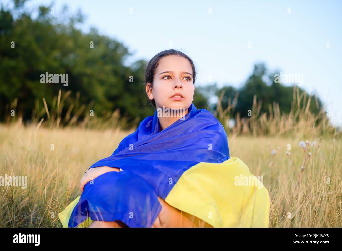 Unrecognizable teen girl sitting in meadow and drawing in