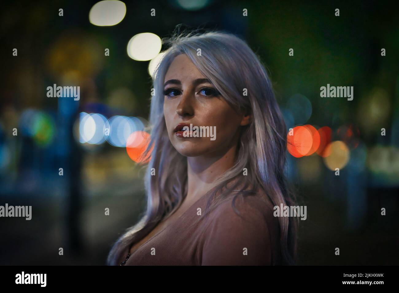 A closeup portrait of an attractive woman in the streets at night with a blurry bokeh background Stock Photo