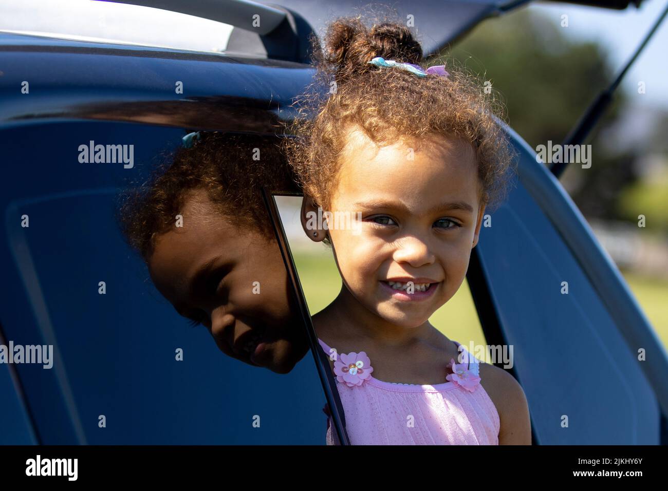 A closeup shot of an African smiling girl reflecting on car window glass on a sunny day Stock Photo