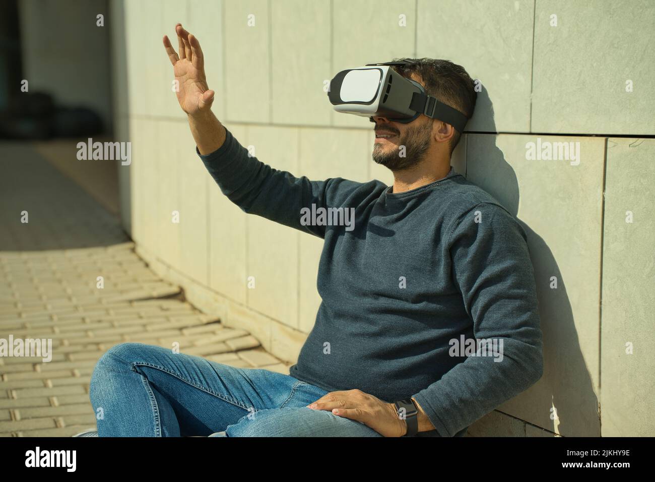 Smiling man using virtual reality (VR) glasses outdoors on a sunny day Stock Photo