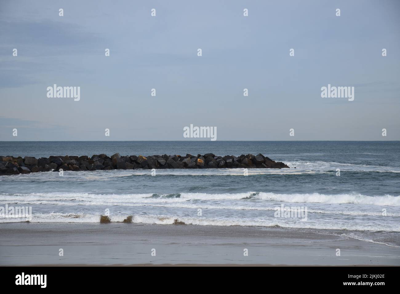 A view from a shore to some stones in the sea looks like wave breakers. Stock Photo