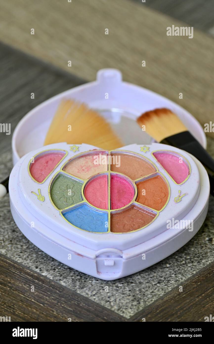closeup the white plastic multicolor makeup kit with brown color brush over out of focus grey brown background. Stock Photo