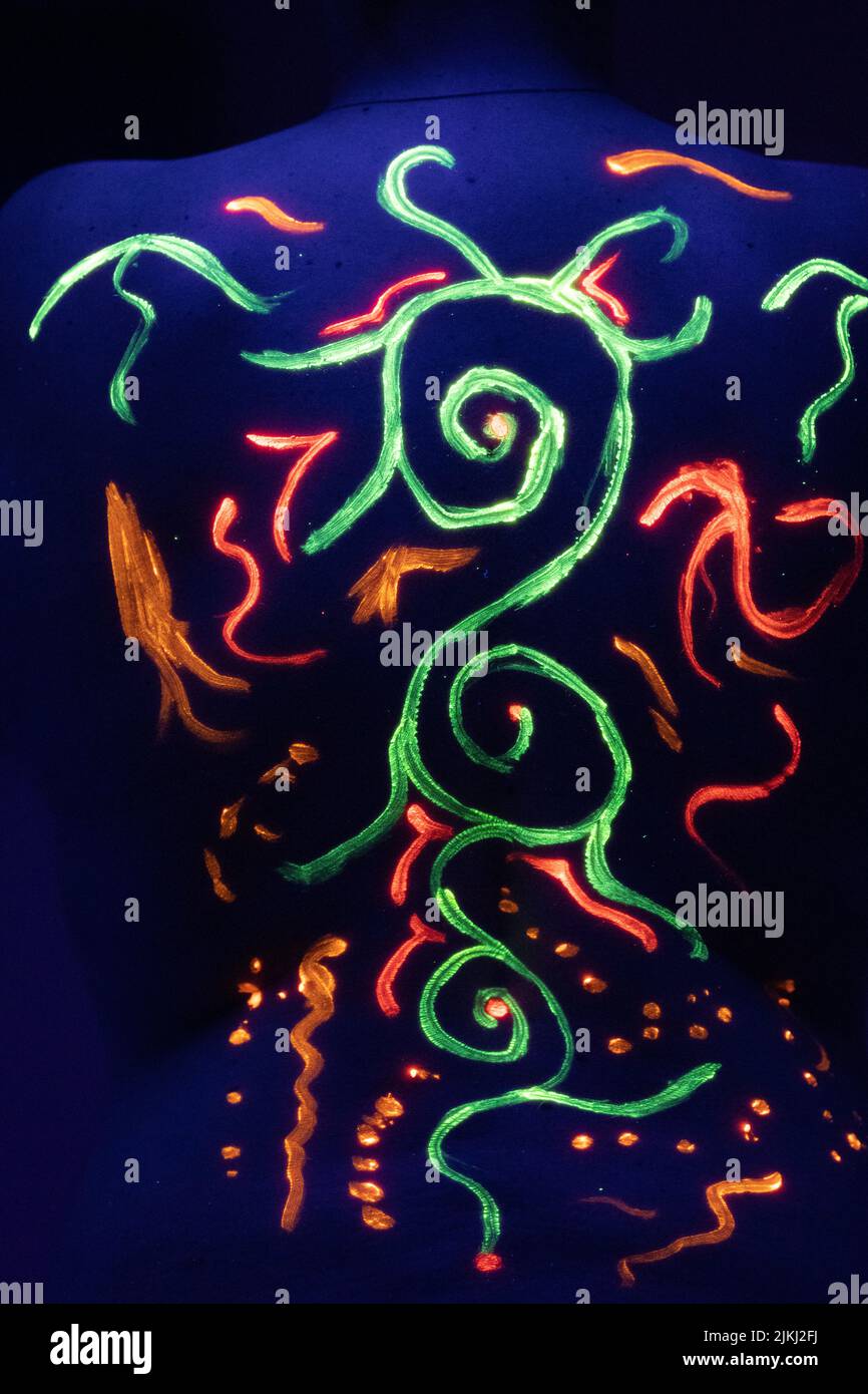 A vertical shot of a female back with colorful ethnic fluorescence patterns art in neon lights Stock Photo