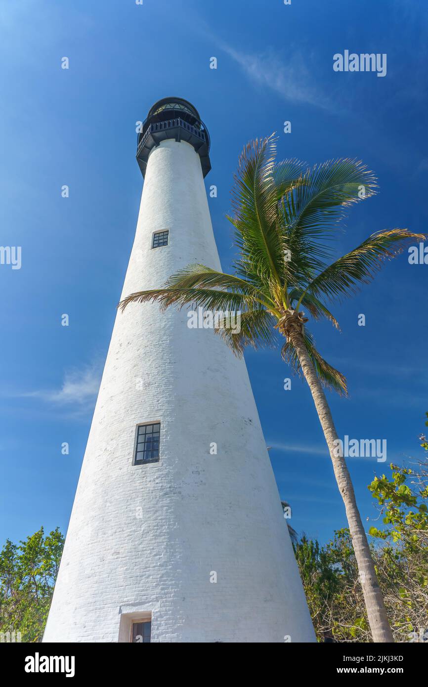 A low angle of the tall white painted lighthouse under the cloudy blue ...