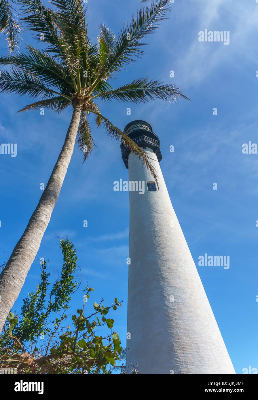 A low angle of the tall white painted lighthouse under the cloudy blue ...