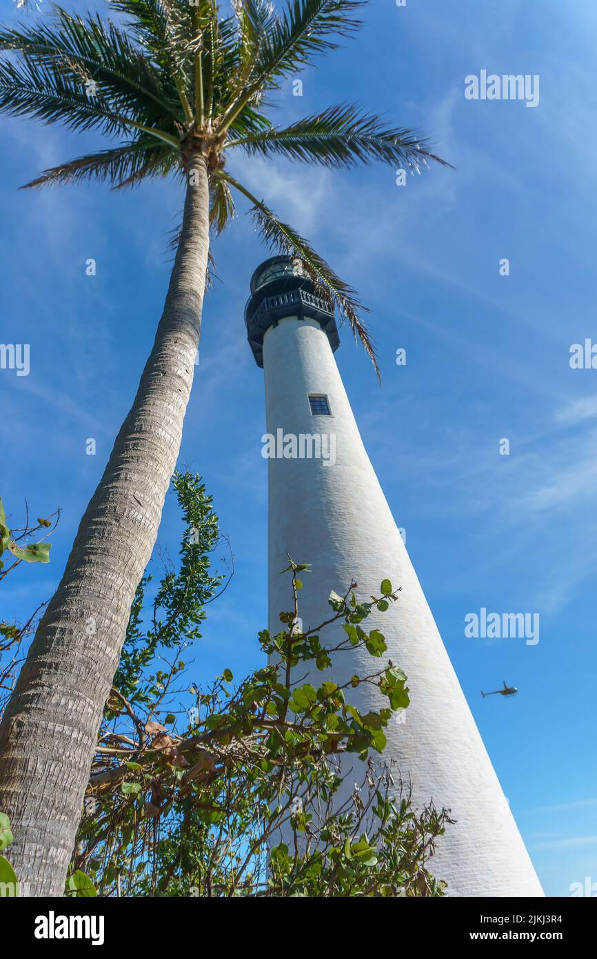 A low angle of the tall white painted lighthouse under the cloudy blue ...