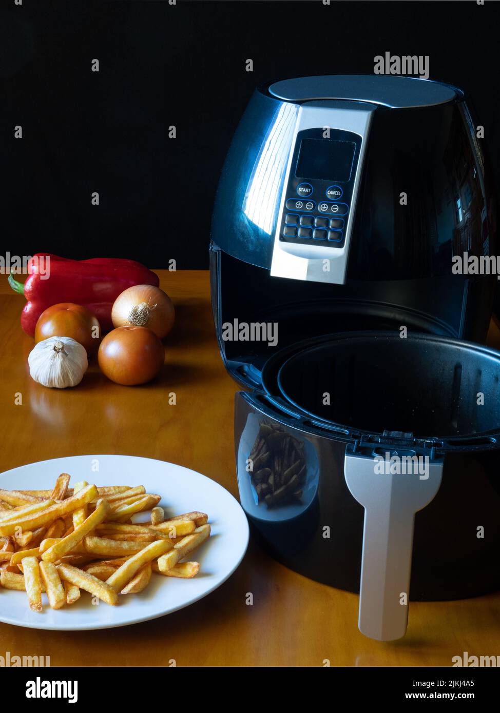 Open air fryer with basket on a table with french fries and vegetables