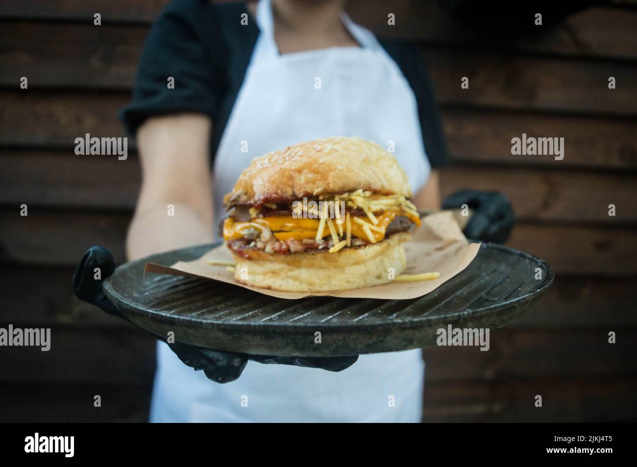 A close-up shot of a chef holding a burger on a black ceramic plate. Stock Photo