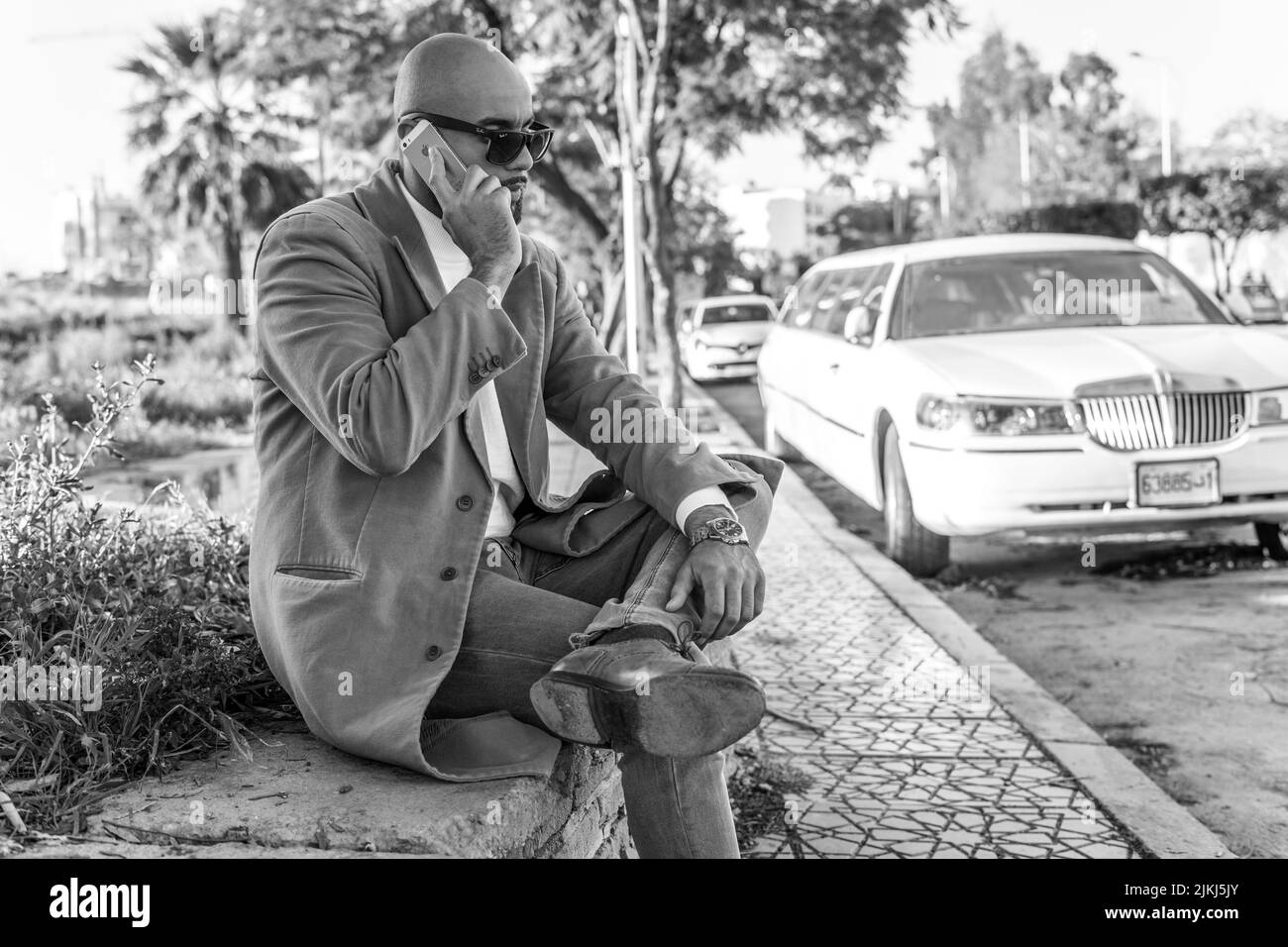 Black and white shot of a man talking on the phone with a limousine car outdoors Stock Photo
