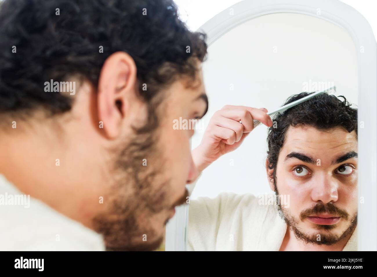 Arab person with beard grooming in bathroom at home. Young man worried for hair loss and looking at mirror his receding hairline. Stock Photo