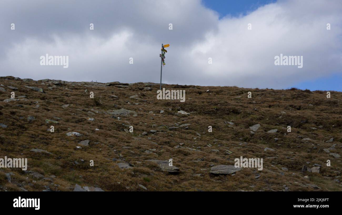 A bottom shot of a signpost stuck on the hill in the background of the cloudy sky. Stock Photo