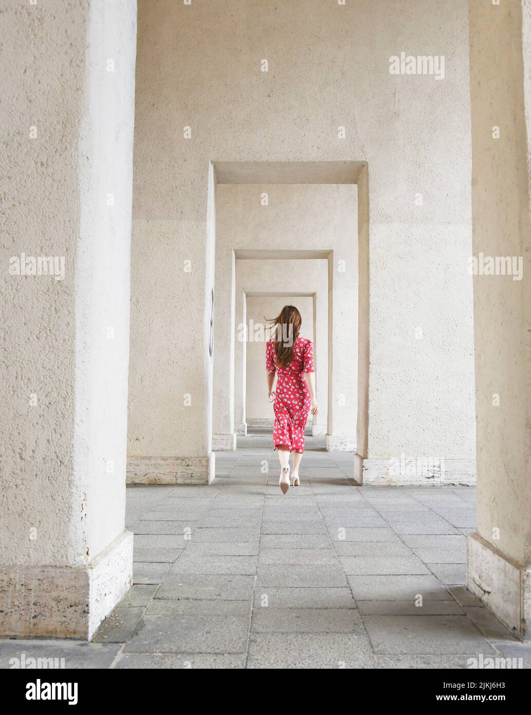 woman in red dress, portico, walking, from behind Stock Photo