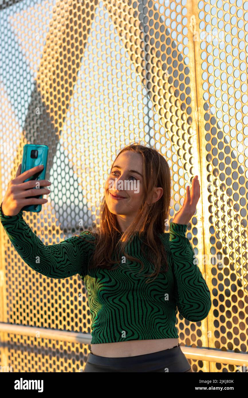 Smiling female making video call on sunset, looking at smartphone screen and talking with friends,family, couple... Vertical portrait Stock Photo