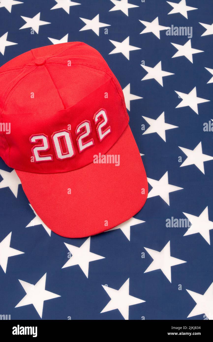 Red MAGA-type hat with 2022 date on US Stars and Stripes flag. For Republican wins in 2022 US Midterm elections in November & US Republican Red Wave. Stock Photo