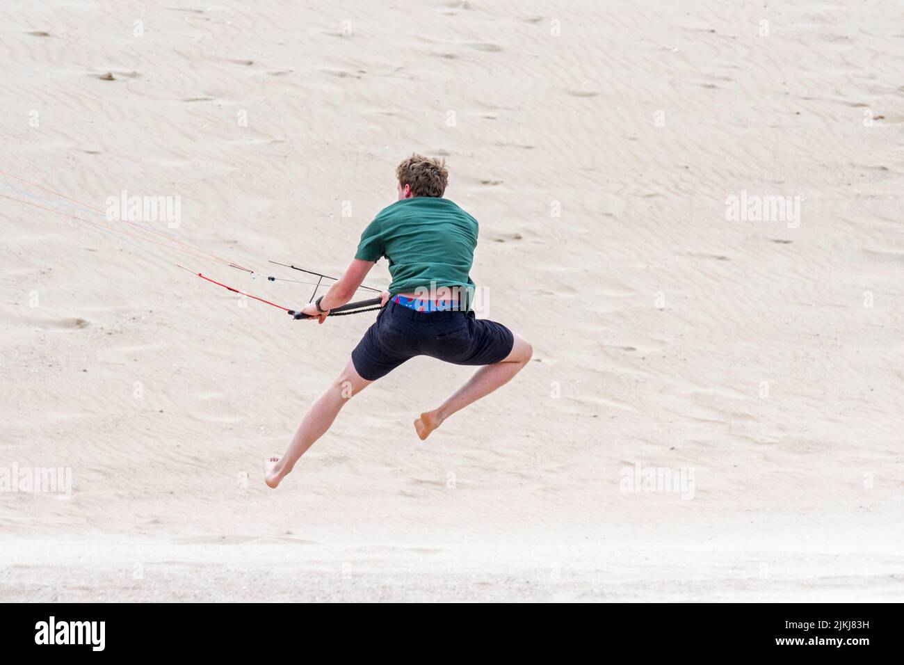 Young man handling 4 line control bar of a flying quad lines trainer parafoil / 4 line stunt kite on sandy beach in strong wind in summer Stock Photo