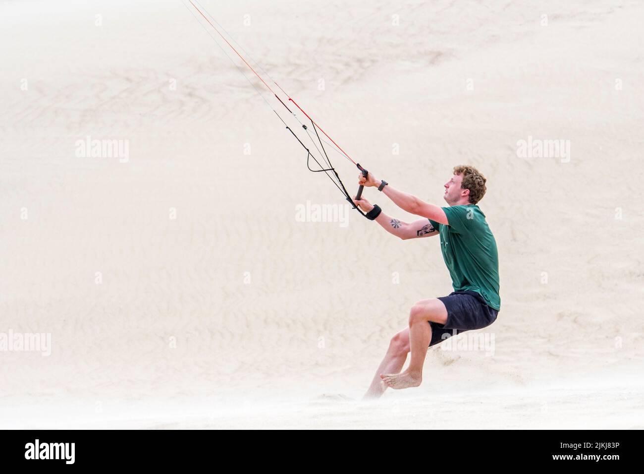 Young man handling 4 line control bar of a flying quad lines trainer parafoil / 4 line stunt kite on sandy beach in strong wind in summer Stock Photo