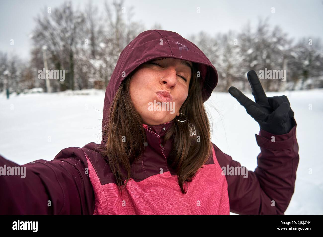 A closeup shot of a happy Caucasian female raising a victory sign with snow ground and trees around Stock Photo