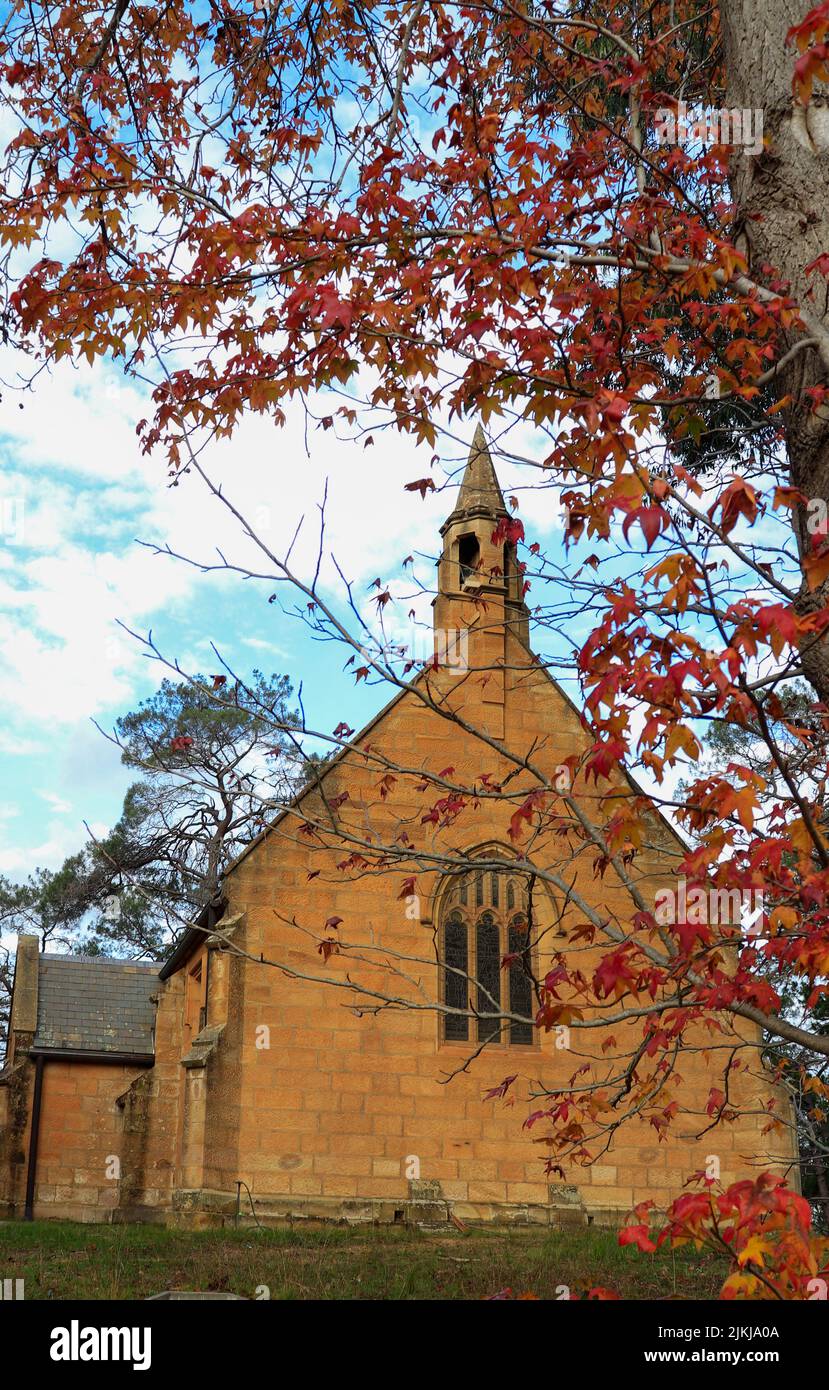 A vertical shot of the Holy Trinity Anglican Church, and red leaves, Berrima Southern Highlands, NSW, Australia Stock Photo