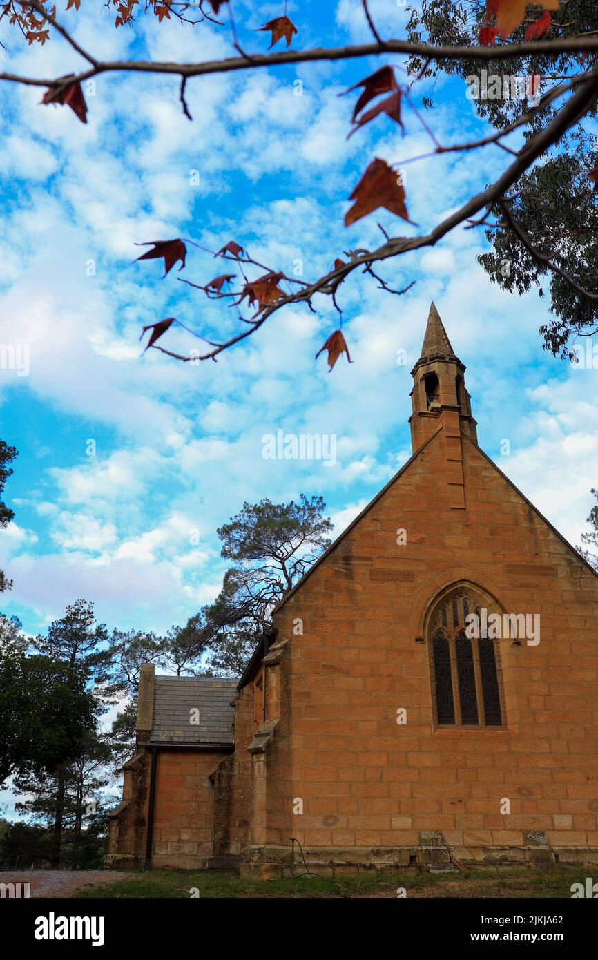 A vertical shot of the Holy Trinity Anglican Church with some red leaves in the foreground, Berrima Southern Highlands, NSW, Australia Stock Photo