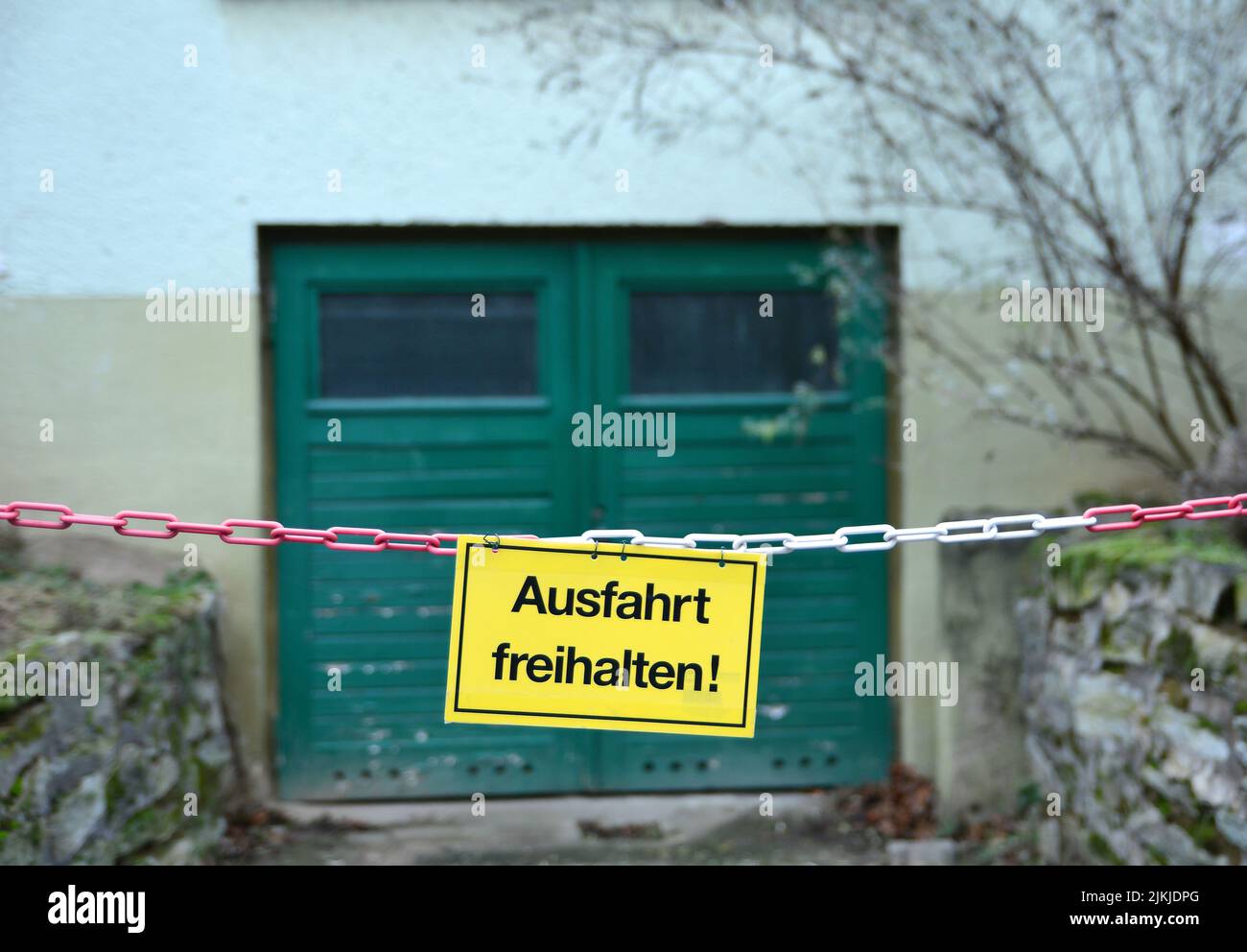 A yellow sign fixed on a chain, with the German words for Keep gateway clear (German: Ausfahrt freihalten) in front of a Garage entrance Stock Photo
