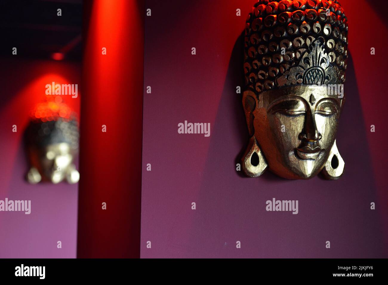 A closeup shot of a large buddha head hanging on the wall with a red light Stock Photo