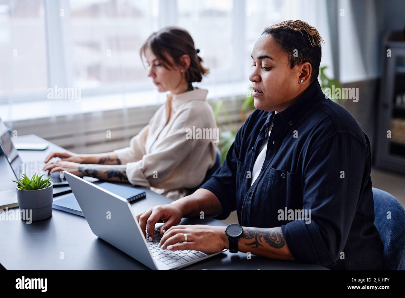 Portrait of two modern women using laptops while working in office together Stock Photo