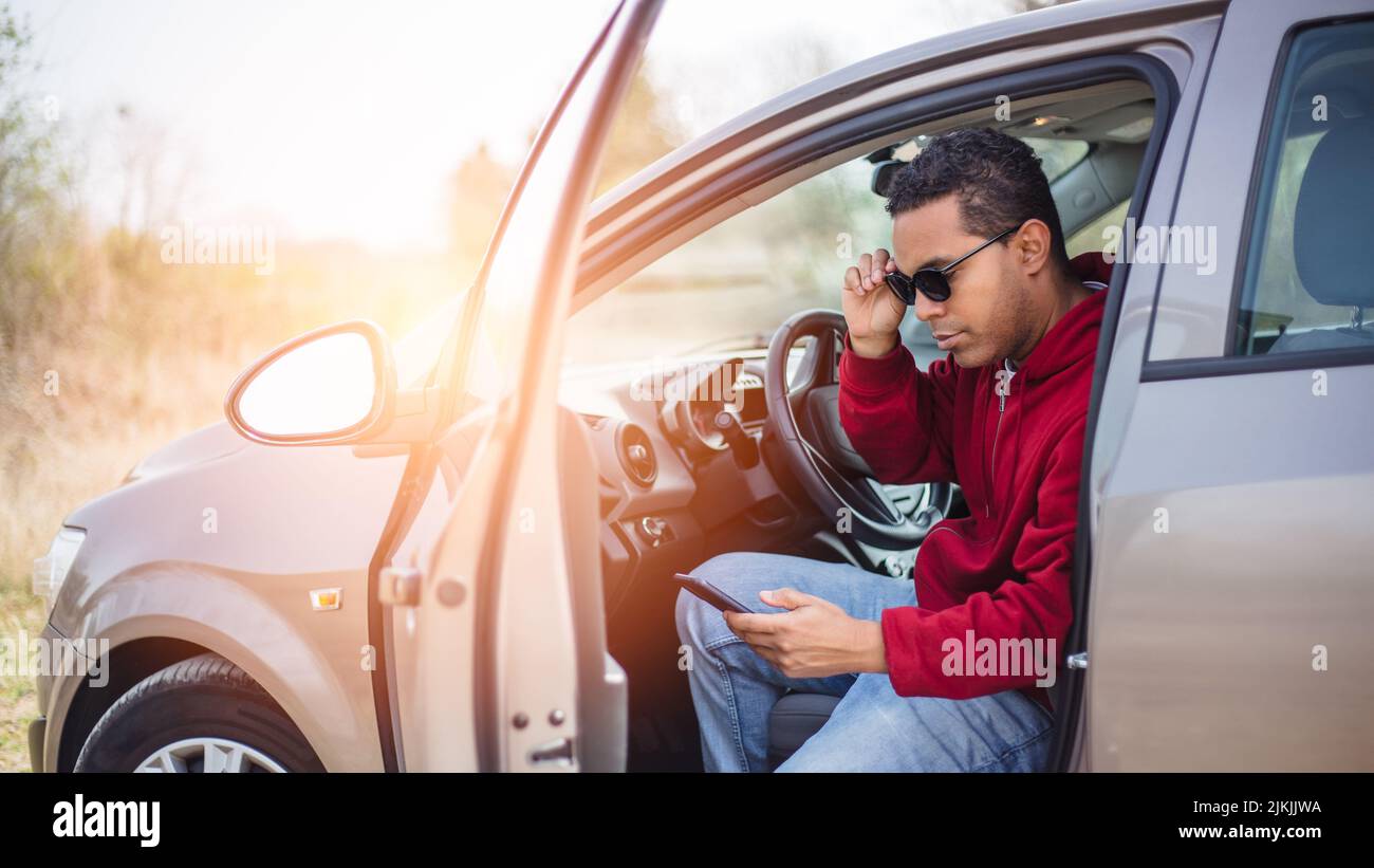 handsome young Hispanic using his car and looking at his smart phone Stock Photo