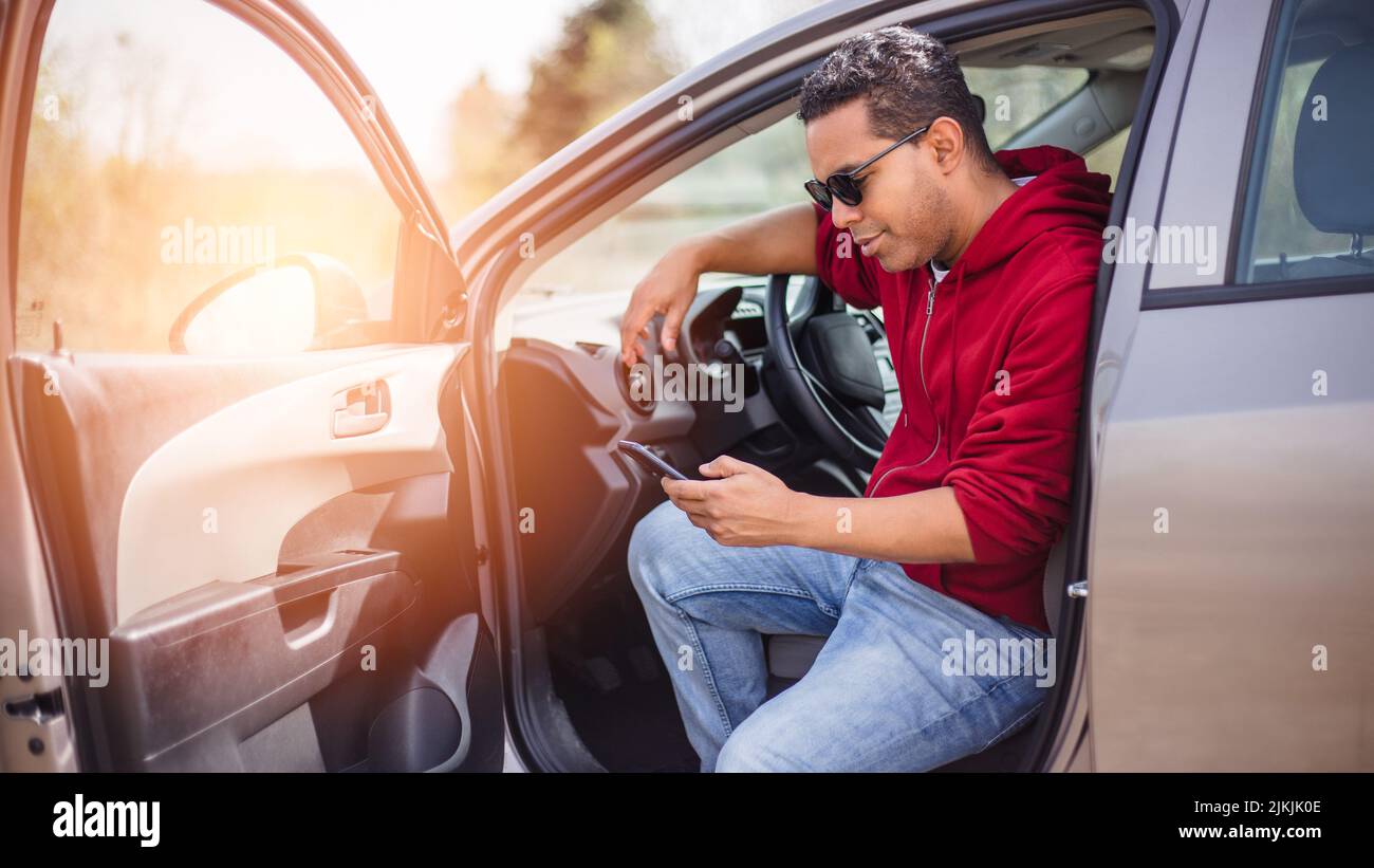 handsome young Hispanic using his car and looking at his smart phone Stock Photo