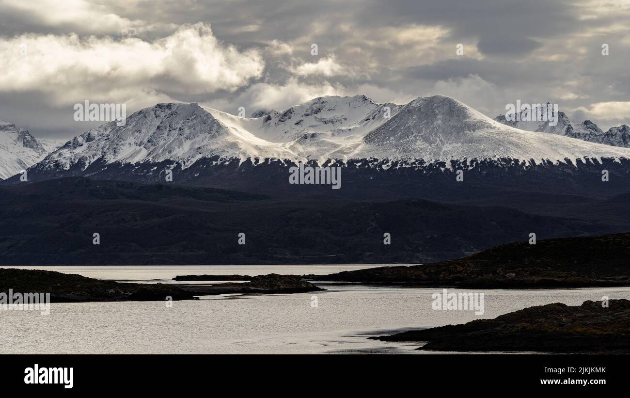 a panoramic shot of lake against snow covered mountains in Ushuaia Stock Photo
