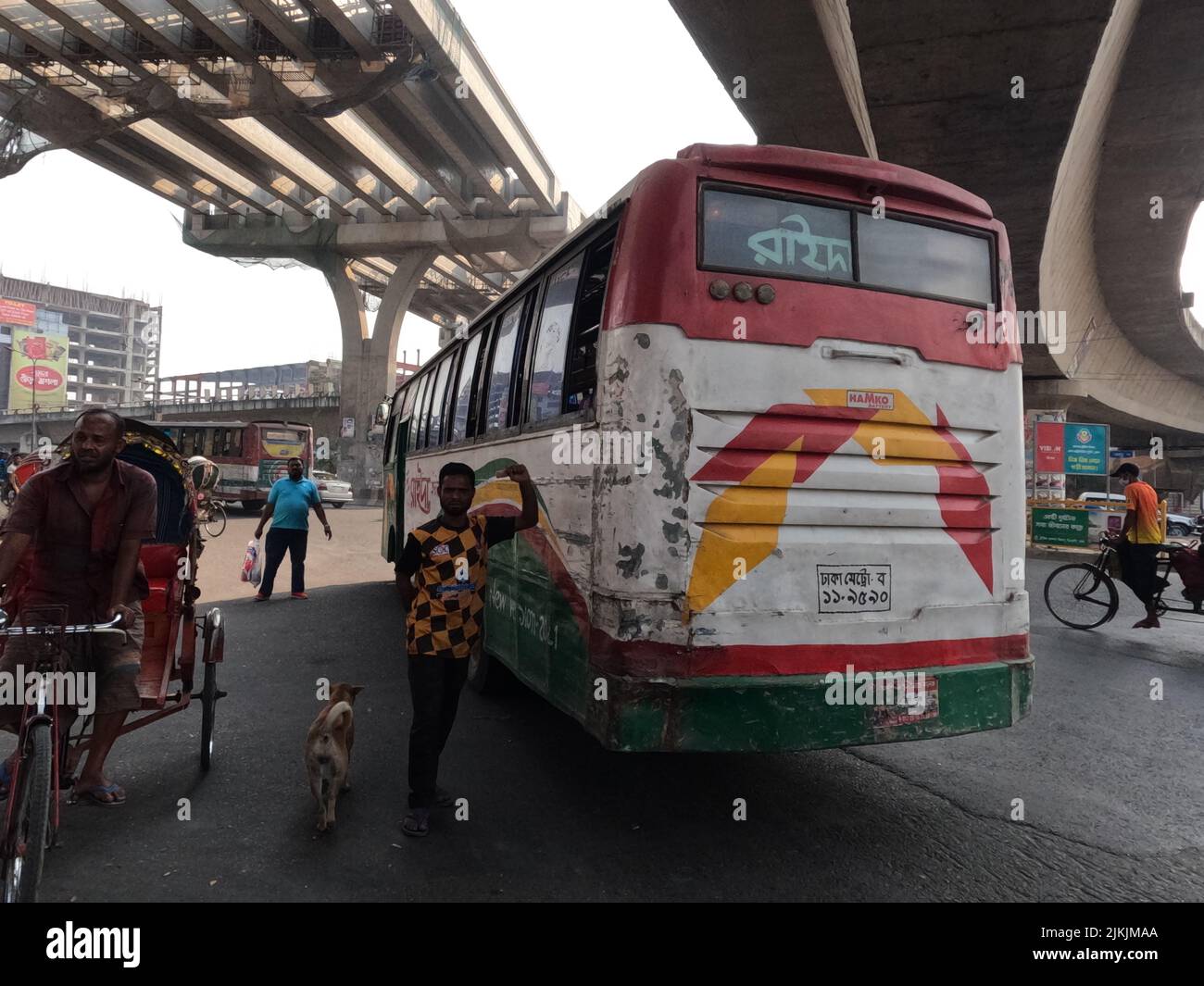 A beautiful shot of males, a dog, and a Rickshaw Puller next to a big colorful transport bus in Dhaka, Bangladesh Stock Photo