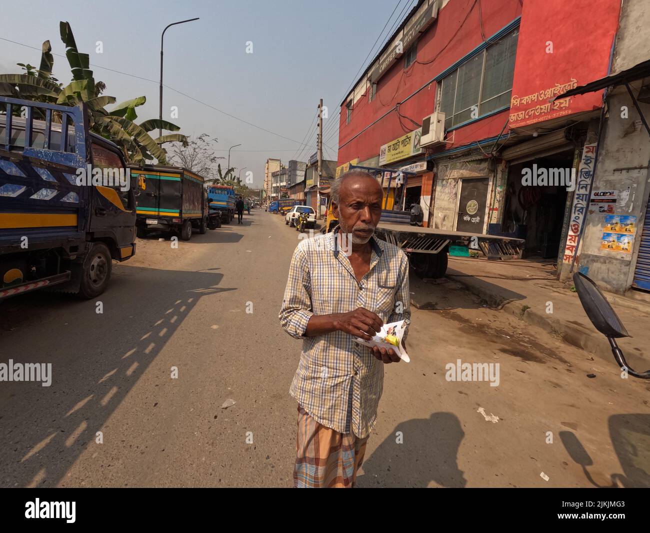 A poor old male eating in the street in Dhaka City, Bangladesh on a sunny day Stock Photo