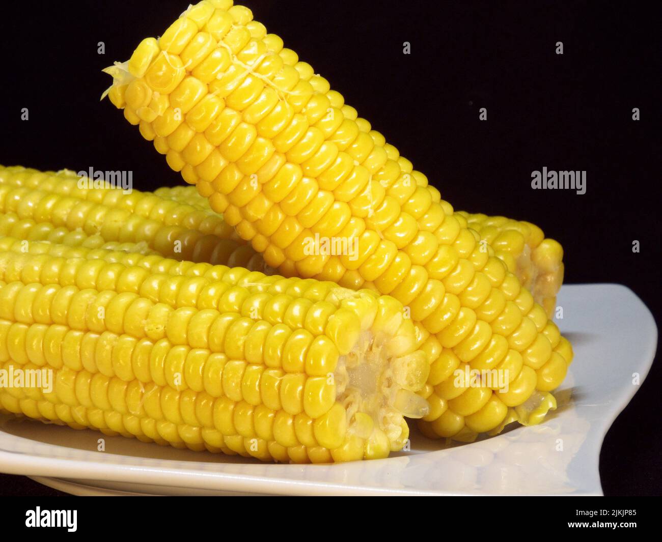 White plate on the 3 husked corn on the cob are Stock Photo