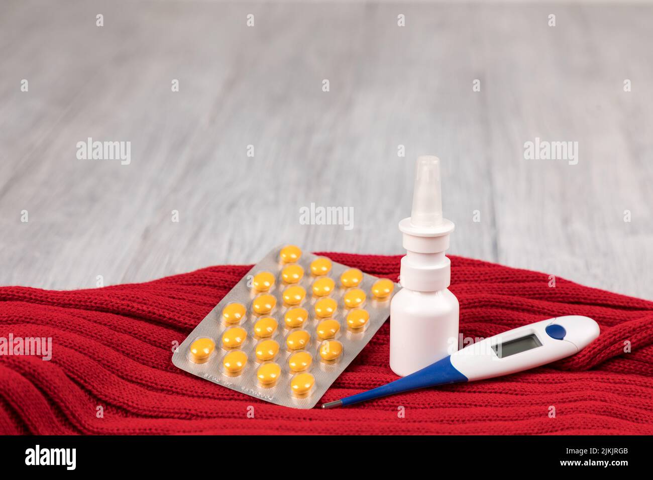 A closeup of a nasal spray, thermometer and tablets with a red scarf on a wooden surface Stock Photo