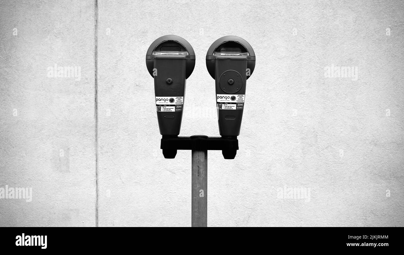 A closeup shot of a parking meter against a wall in black and white Stock Photo