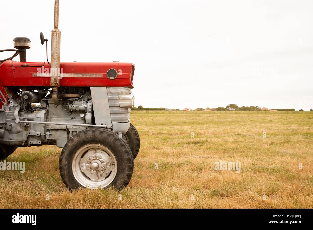 Detail of the front of a tractor standing in a crop field. The day is cloudy. Concept of agriculture and rural life. Space for text. Stock Photo