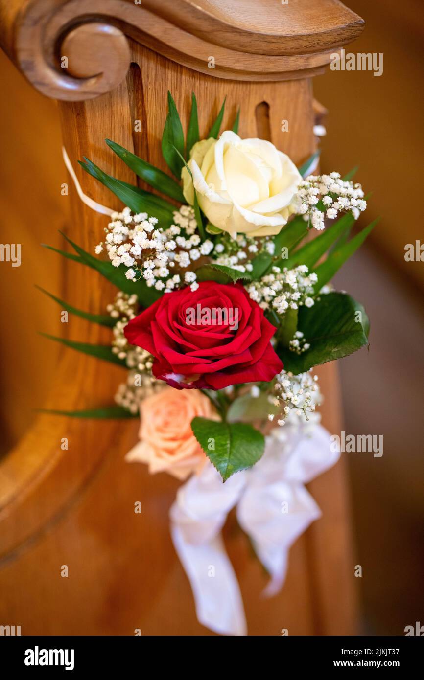 A vertical shot of floral decoration on a wooden bench in the church during a wedding ceremony Stock Photo