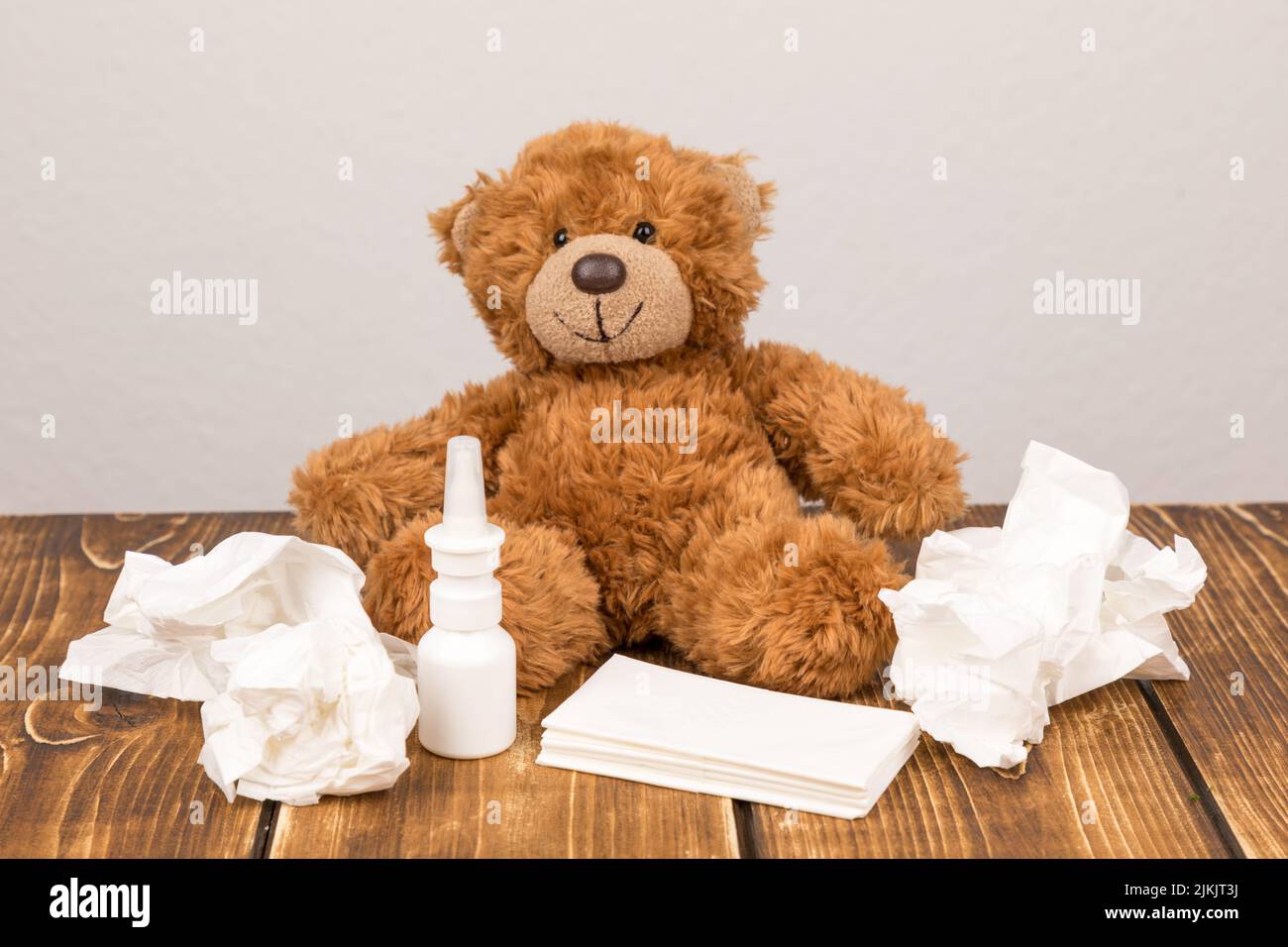 A fluffy teddy bear with a nasal spray and tissues on a wooden surface - suffering from illness Stock Photo
