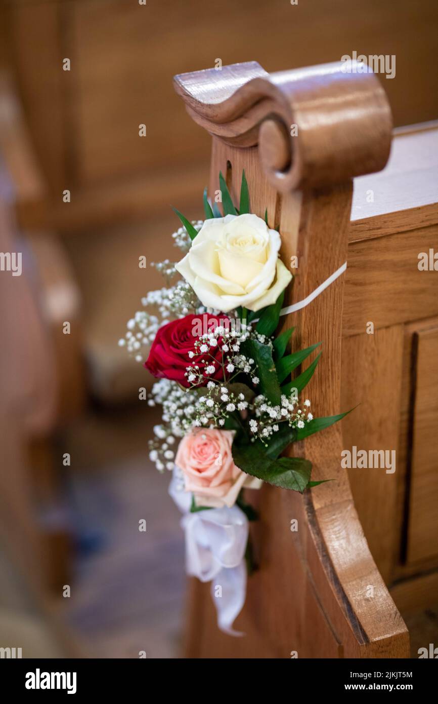 A vertical shot of floral decoration on a wooden bench in the church during a wedding ceremony Stock Photo