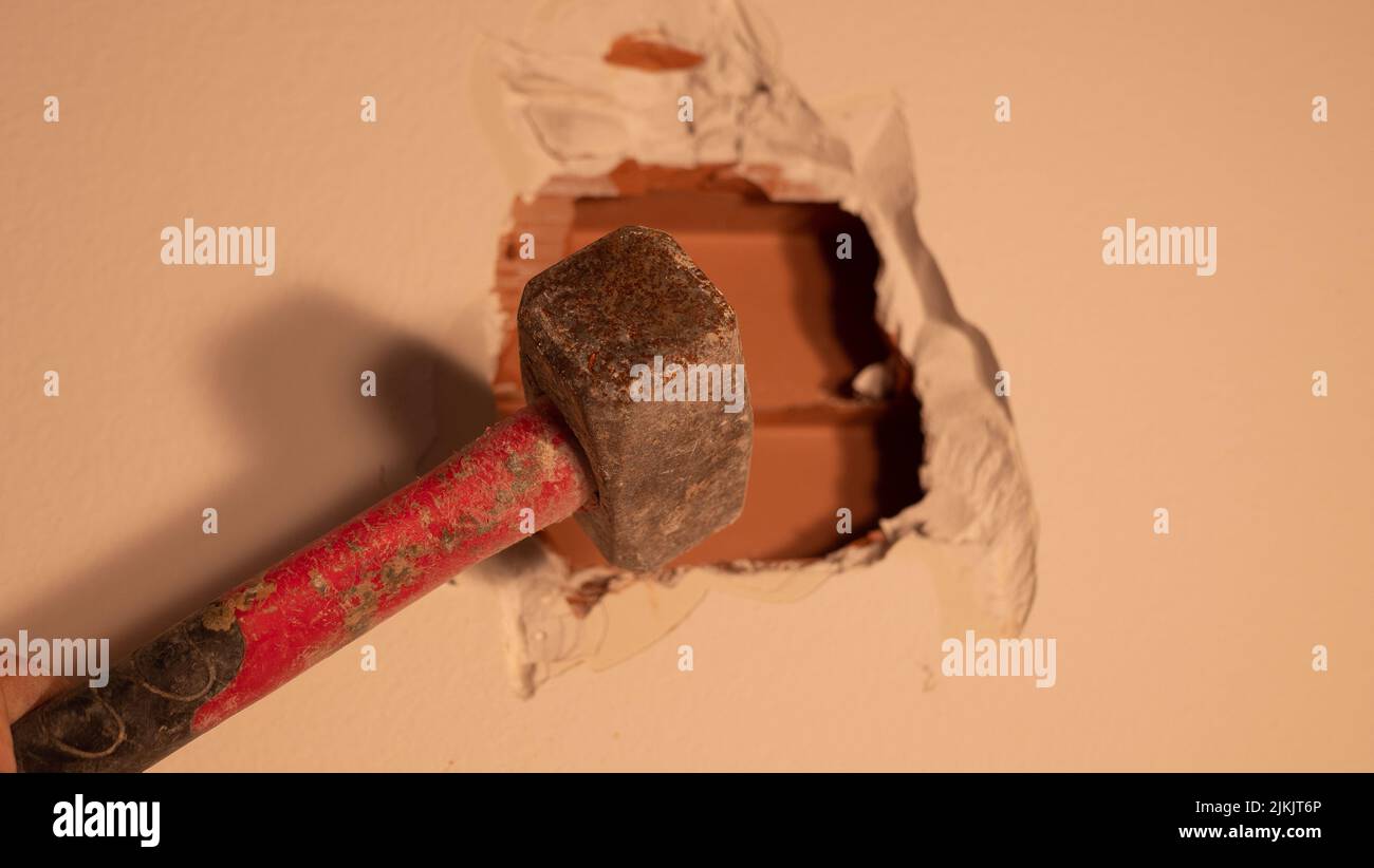 worker with a hammer and chisel makes a hole in the wall at the construction site Stock Photo