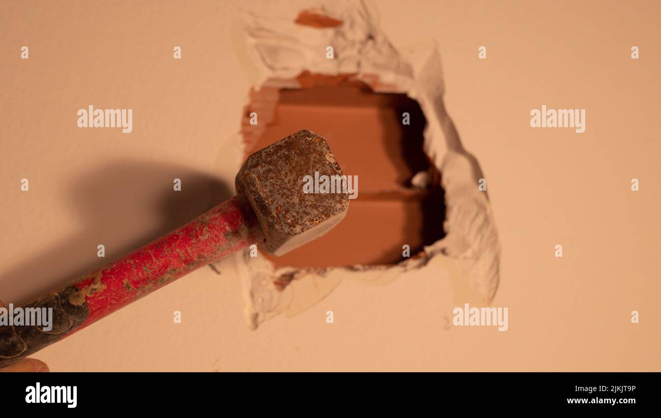 builder punches a hole in the wall with a hammer, close up Stock Photo