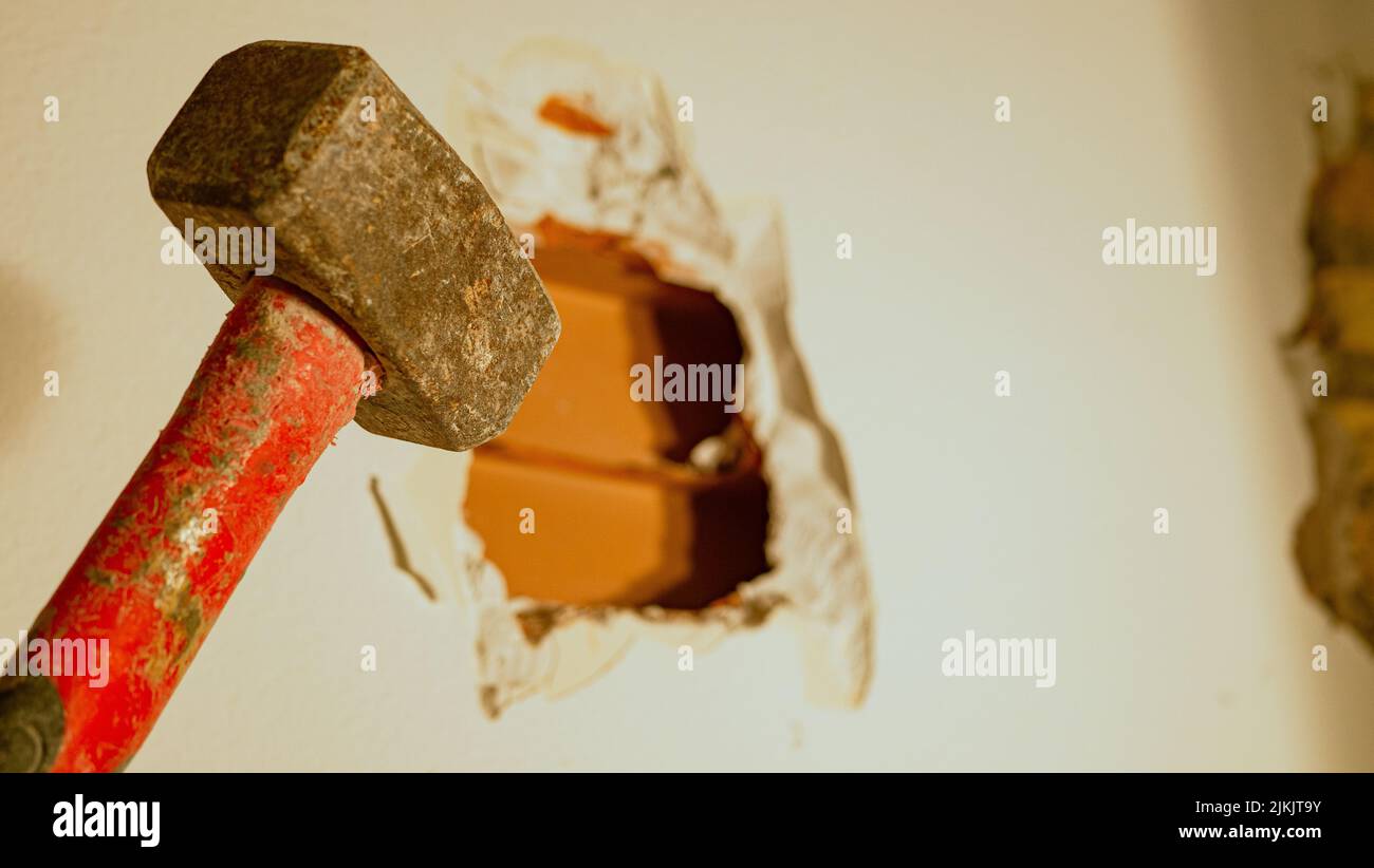 builder punches a hole in the wall with a hammer, close up Stock Photo