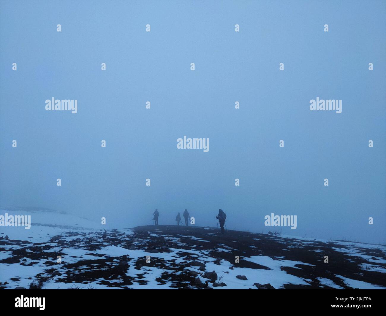 A group of people hiking in the mountains covered in snow on a foggy evening Stock Photo