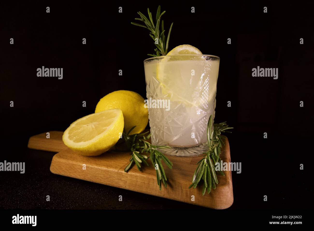 A closeup shot of a rosemary lemon gin tonic on a cutting board isolated with black background Stock Photo