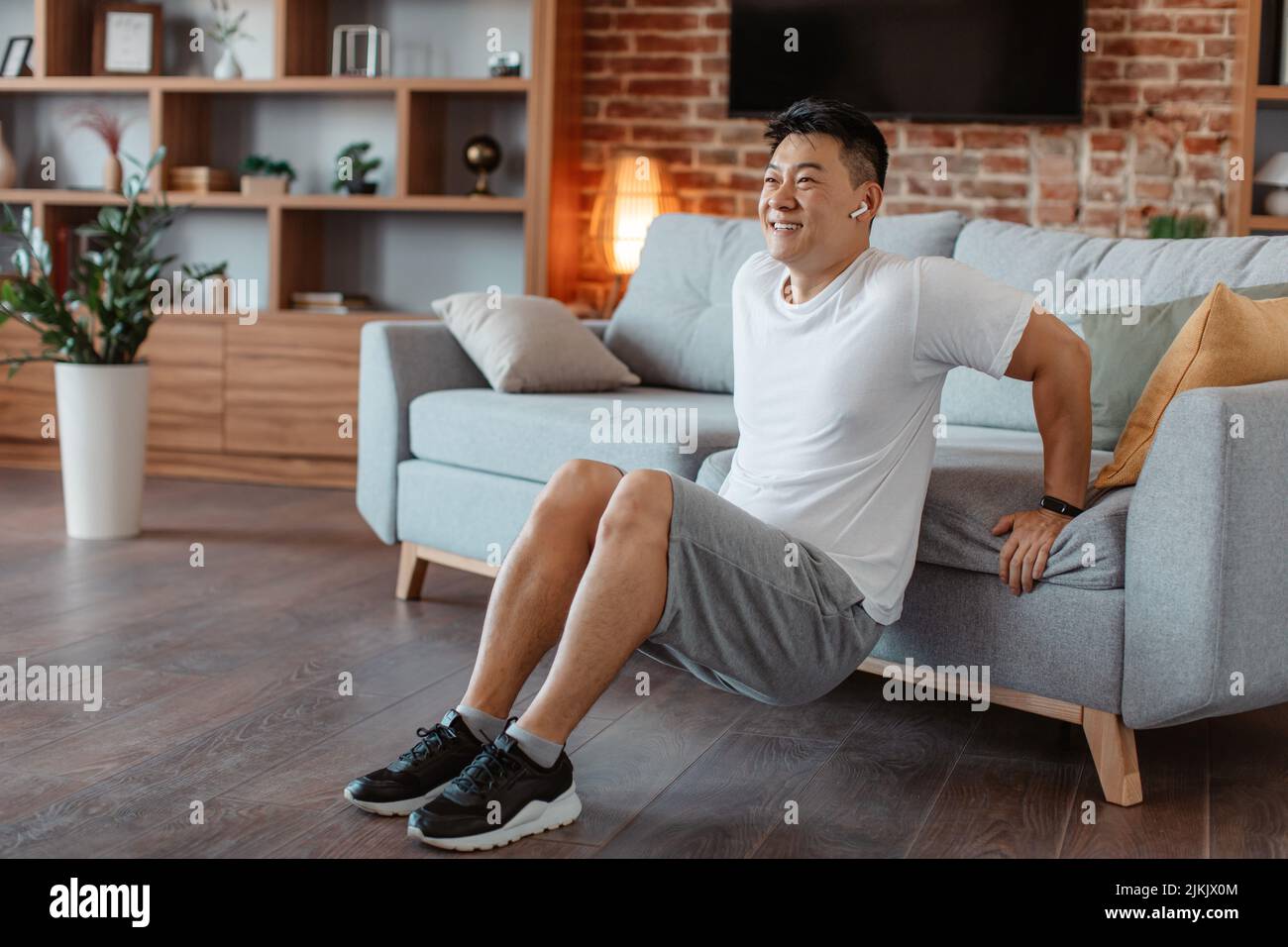 Home training to keep fit. Sporty middle aged asian man leaning on sofa