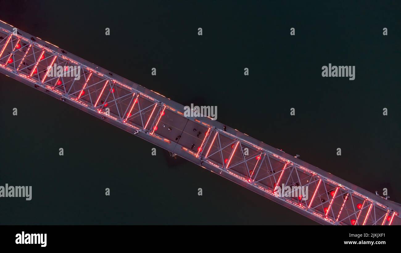 An aerial view of a bridge with illuminated red lights over a river at night Stock Photo