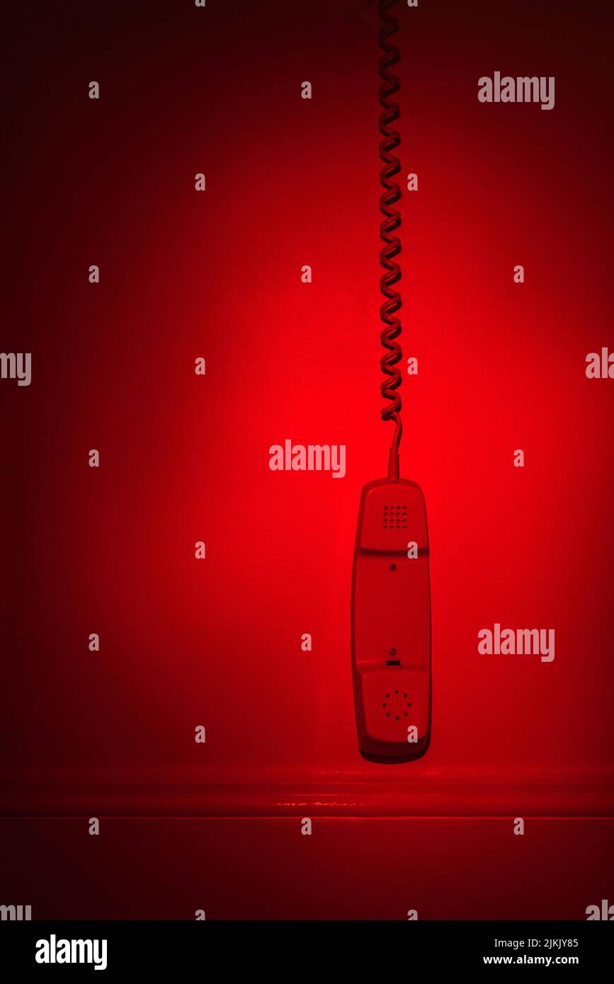 Intercom phone off the hook and dangling along a wall in red light Stock Photo