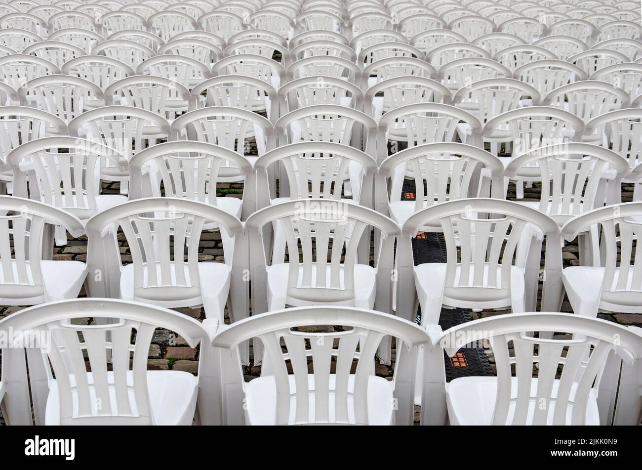 Seemingly endless number of rows of white plastic chairs in an outdoor setting Stock Photo