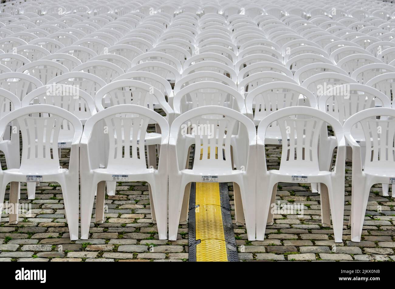 Rows of white plastic chairs on a cobblestone pavement with a cable tray Stock Photo