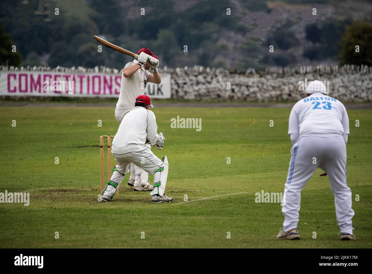 Cricket Batsman about to hit the ball, watched by a wicket keeper and fielder during a weekend local village cricket match in Huddersfield, Yorkshire Stock Photo